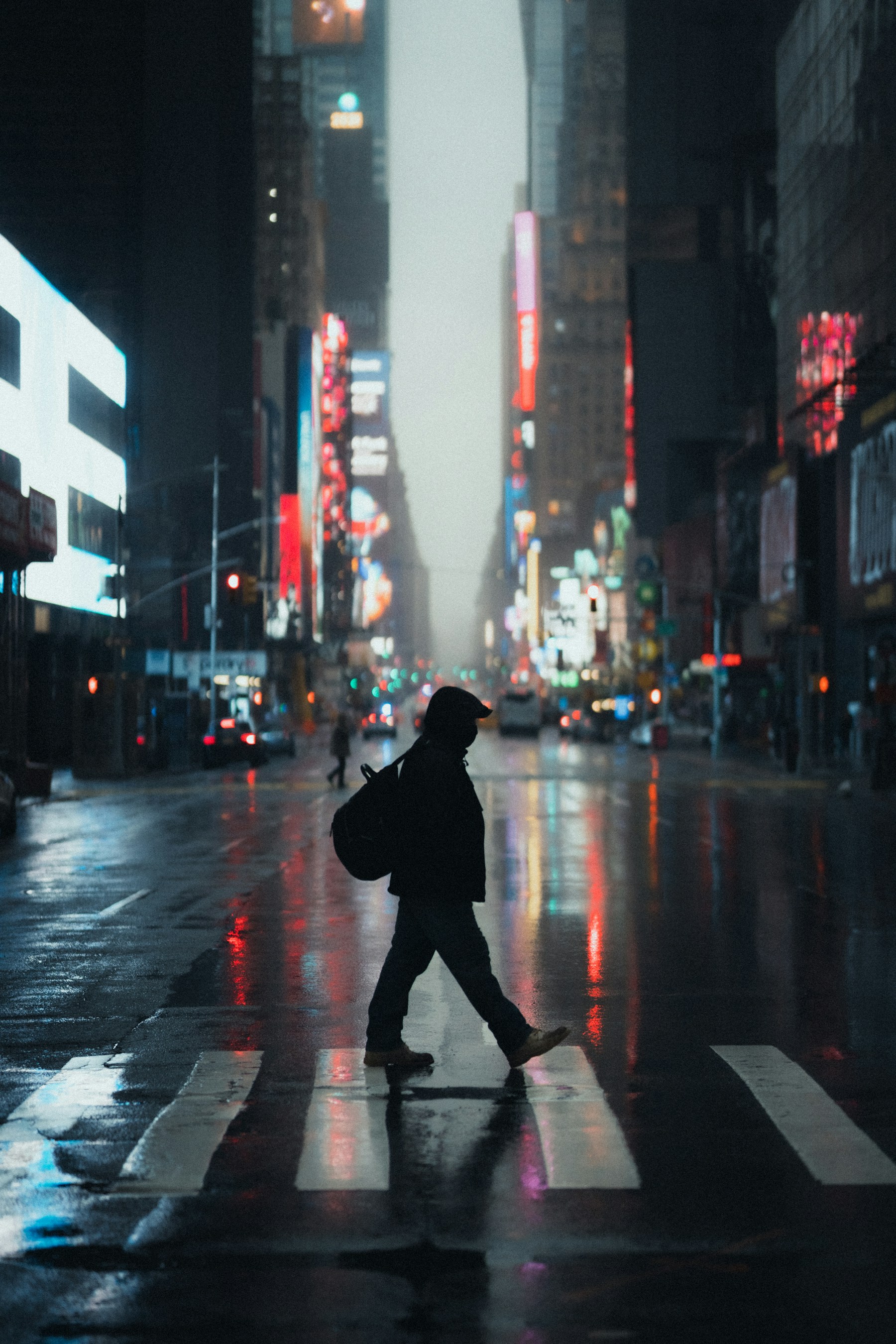 Silhouette crossing a luminous city street in the rain